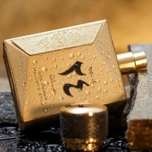 Gold perfume bottle with water droplets on a textured surface