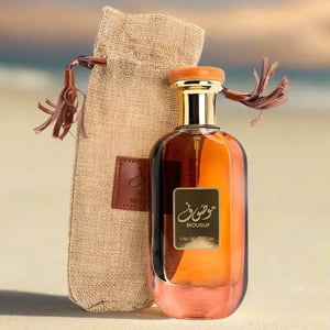 Perfume bottle with 'Mousuf' branding next to a textured bag on a blurred background