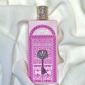 Perfume bottle with pink packaging featuring decorative elements on a white fabric background