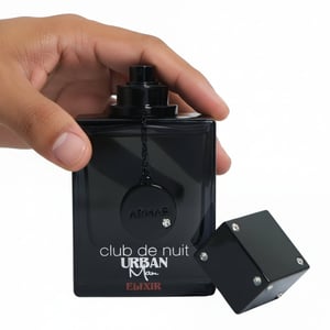 Hand holding a black perfume bottle labeled 'Urban Man Elixir' with its packaging on a white background.