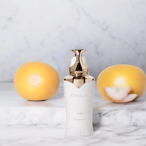 White skincare bottle with gold cap on a marble surface with two yellow fruits.