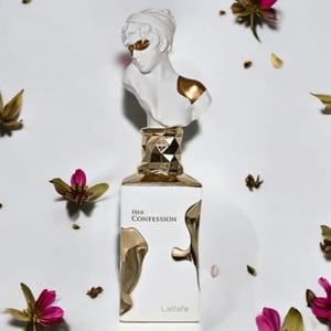 Perfume bottle labeled 'Her Confession' with decorative bust on a light background with flowers.