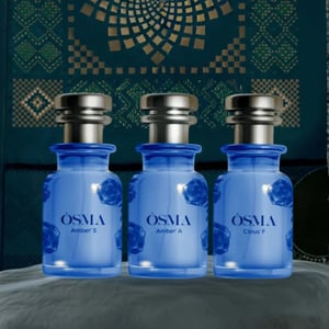 Three blue bottles labeled 'OSMA' on a textured surface with a patterned background.