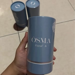 Blue cylindrical container with 'OSMA' branding held by a hand on a tiled floor.