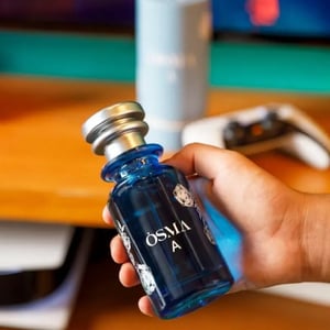 Hand holding a blue bottle labeled 'Osmia' with a blurred background