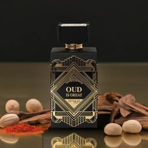 Perfume bottle labeled 'Oud is Great' with decorative elements on a reflective surface.