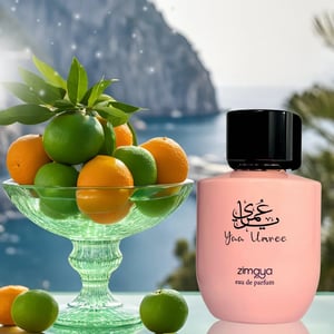 Pink Zimaya eau de parfum bottle with a bowl of oranges and limes against a scenic background.